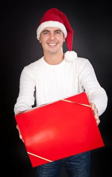 Smiling man in Santa hat gives a red box in the studio against a dark background