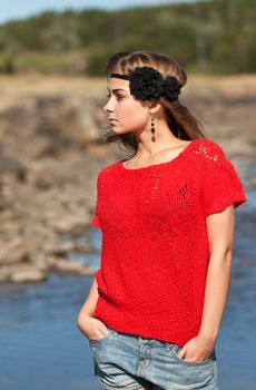 Beautiful girl in a red sweater and denim shorts on the rocks in a forest