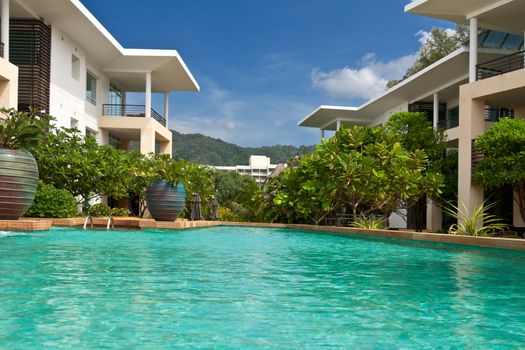 Hotel with sky-blue swimming pool with palm trees against the mountain