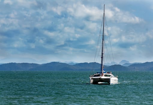 white catamaran with a flat sail against the backdrop of tropical islands