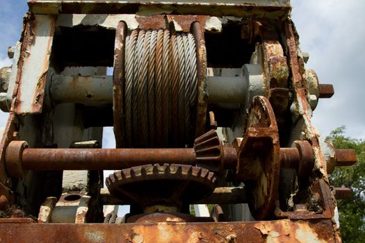 Rusty metal housing with a metal cable coil and winding gear.