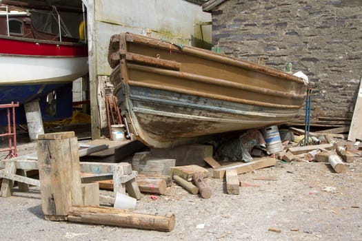 The hull of a wooden boat undergoing restoration in a wok yard with a variety of supports.