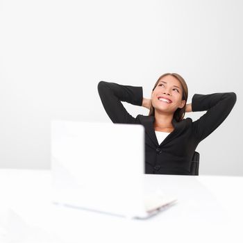 Thinking office worker day dreaming looking up smiling happy. Young business woman in suit sitting at office desk with laptop. Young mixed race Asian / Caucasian businesswoman.