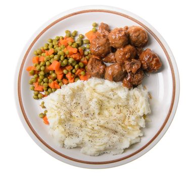 An american supper of mashed potatoes, with sweet and sour meatballs with peas and carrots.