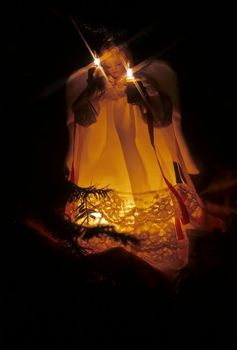 Christmas holiday tree ornament - lighted angel holding two candles lit with bulbs and light rays.