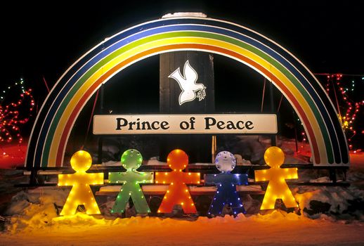 Lighted Christmas display - rainbow, dove, prince of peace sign, colored figurines and colored lights photographed at night in the snow.