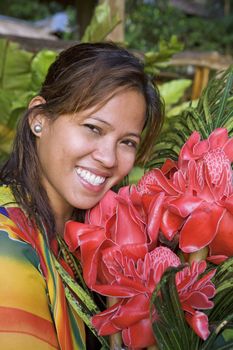 Beautiful, young, Asian woman from the Philippine Islands posing with exotic, tropical red ginger lily flowers and a beautiful smile with bright, white teeth.
