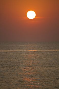 View of a big red sun at sunset on a calm beach.