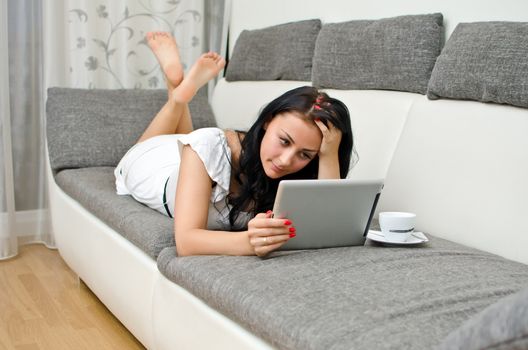 Brunette girl with tablet pc on the sofa.