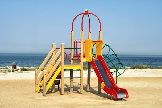 Colourful wooden childs slide and playground on a deserted sandy beach at the seaside on a sunny summer day