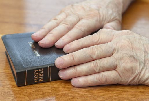 old man hands on bible over table