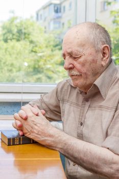 Old man praying at home near the window