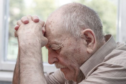 Old man praying at home near the window