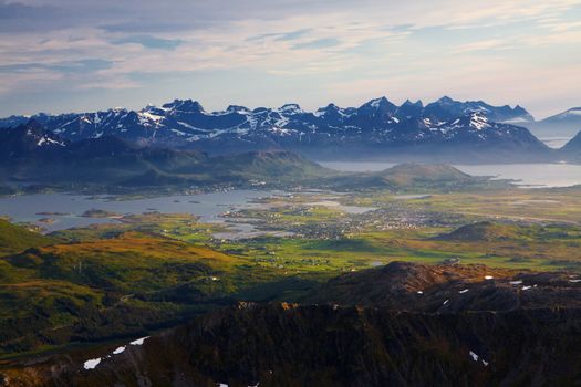 Picturesque panorama on Lofoten from Justadtinden with green lowlands and snowy peaks of mountains