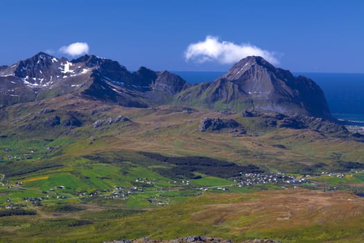 Picturesque panorama on Lofoten from Justadtinden with green lowlands, snowy peaks of mountains and Atlantic ocean in the background