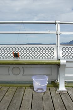 A crab line reel attached to a seat railing with a clear plastic bucket with a crab in water.