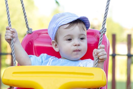 9-month old baby boy with blue hat in a swing outdoors