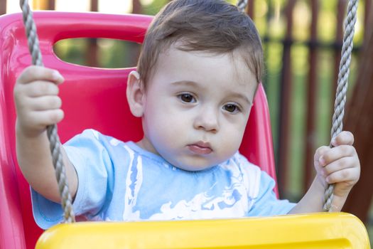 close-up of 9-month old baby boy  in a swing outdoors