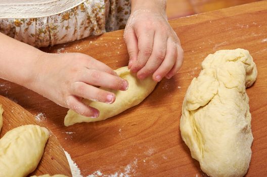 Smiling little girl kneading dough at kitchen .Detail of hands kneading dough