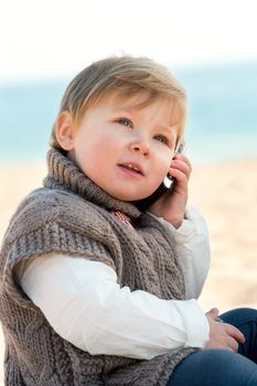 Portrait of cute little girl on beach talking on mobile phone.