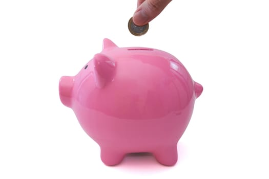 Coin holding by two fingers and pink piggy bank standing on isolated white background.