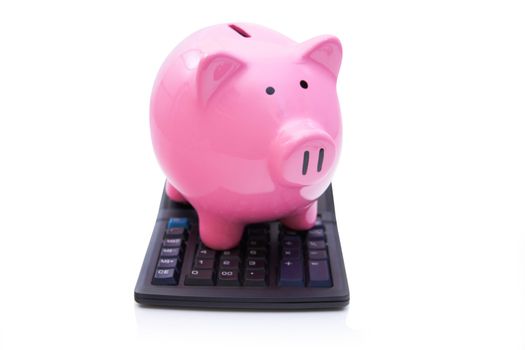 Pink piggy bank is on the calculator on white background.