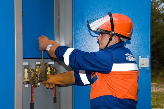 Electrician in blue overalls and a protective helmet off the light at the substation