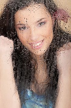 Smiled woman behind glass full of water drops