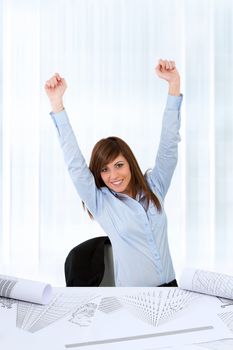 Attractive young business woman at desk raising hands for success.