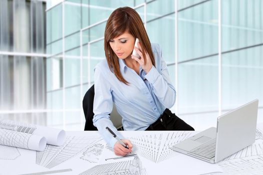 Attractive young female architect working at desk with plans.