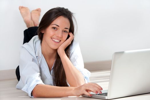 Portrait of young attractive woman laying on floor with laptop.