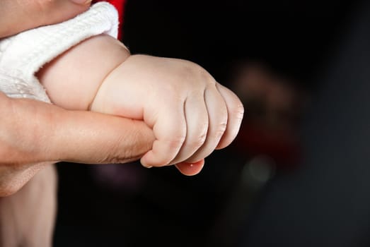 Baby hand holding mother finger on the black background.