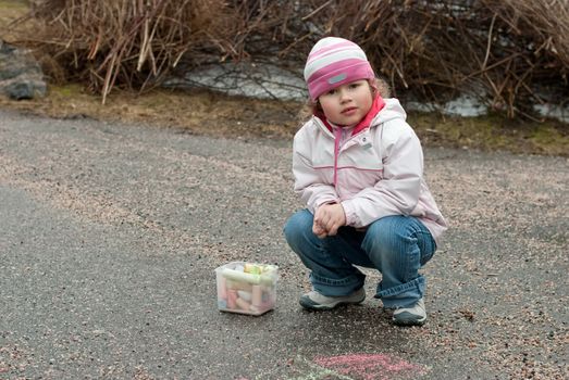 Little girl drawing a chalk on the pavement.