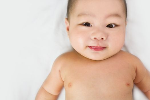 A cute little asian baby staring into the camera sticking out tongue.