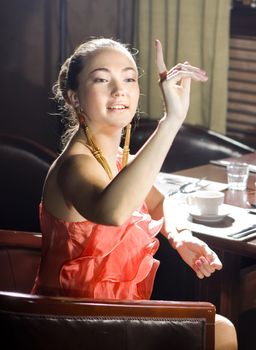 woman sits at the table and does a sign to the waiter at restaurant