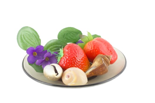 Artificial flowers, strawberries and sea shells on saucer.