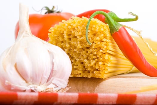 Golden raw dried Italian pasta with other ingredients on kitchen desk.