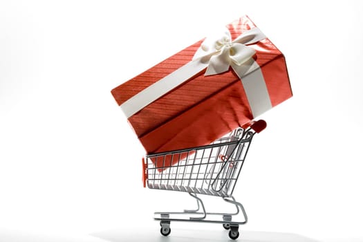 shopping cart with gift box wrapped in colored paper and ribbon on white background