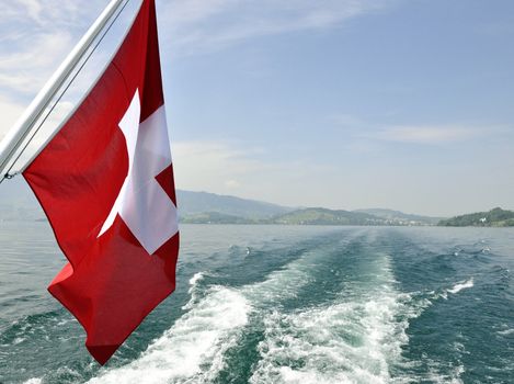 Swiss flag in boat, during summer. Lake and mountains in the back.