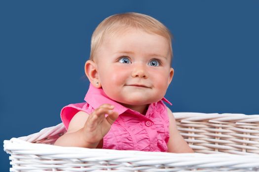 Blue eyed baby girl with staring look sitting in a white basket with a blue background