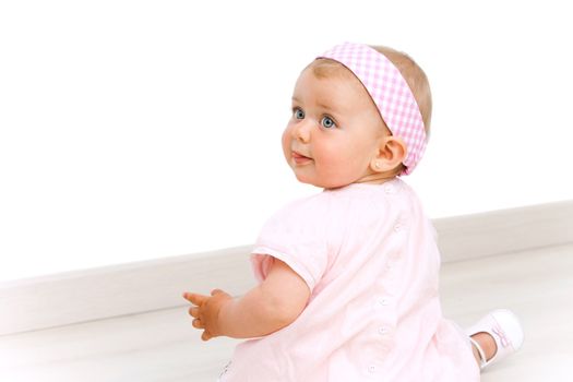 Blue eyed baby girl wearing a pink dress and pink head band sitting on the floor.