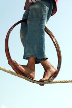 A closeup view of the feet of a poor Indian trapeze girl, whose daily living hangs on the balance of her act on the rope. The image also depicts progress based on the right balance.