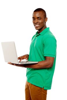 Cool teenage guy surfing internet on laptop and smiling at camera