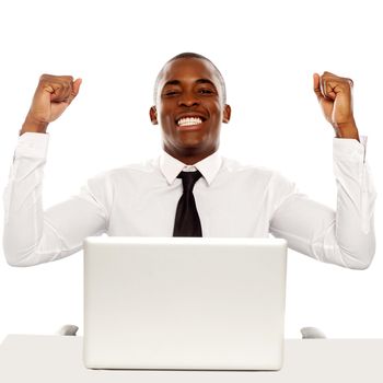 Victorious african business executive raising his hands in excitement sitting in front of laptop
