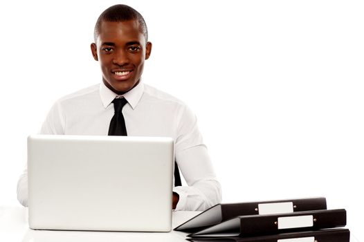African corporate male manager at work desk using laptop and looking at camera