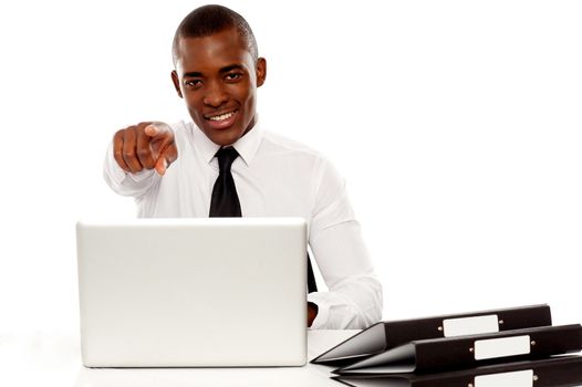 Confident businessman pointing at you while working on laptop isolated over white
