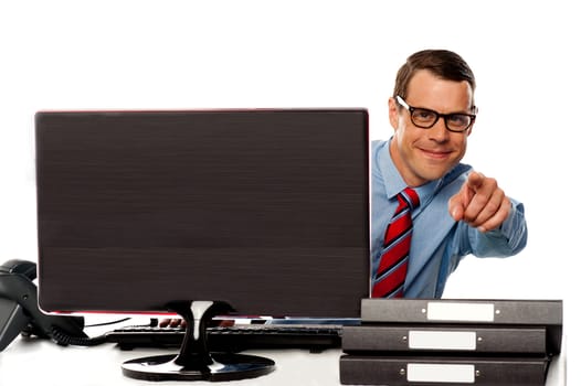 Male executive in glasses pointing at camera sitting in front of computer screen