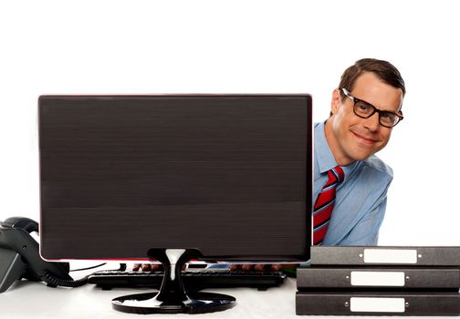 Man peeping from behind computer screen and enjoying at work. Sitting in office