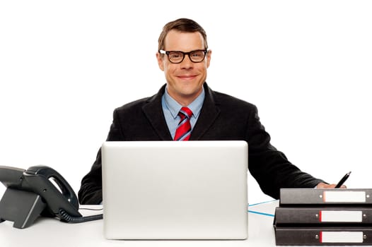 Confident smiling male executive wearing glasses and posing at work desk