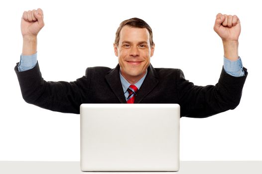 Excited businessman celebrating success with his arms raised up. Sitting in font of laptop